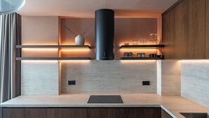 Een moderne keuken met een centrale, zwarte afzuigkap, houten kastjes en verlichting onder de kast.