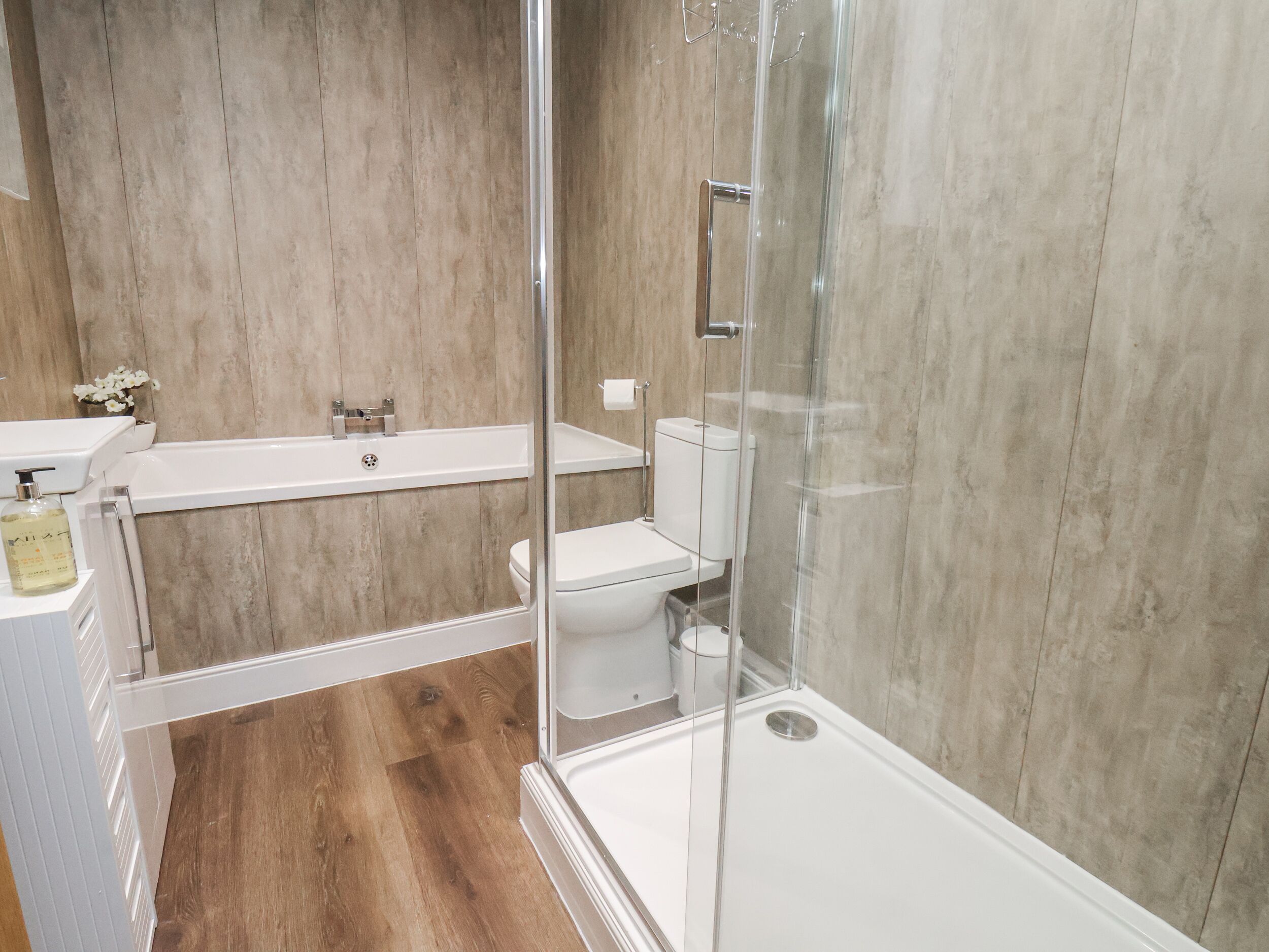 A modern bathroom with a glass-enclosed shower, a white bathtub, and a toilet.
