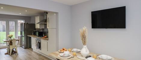 Een moderne keuken met een eethoek, een flatscreen televisie aan de muur en een houten tafel gedekt voor een maaltijd.