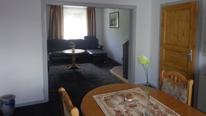 A living room with a sofa, a small table, and a dining table with a vase of flowers. - Vacation cottage Van Wijk (Alheim)