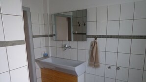 A bathroom with a white sink, wooden vanity, tiled walls, and a mirror. - Vacation cottage Van Wijk (Alheim)