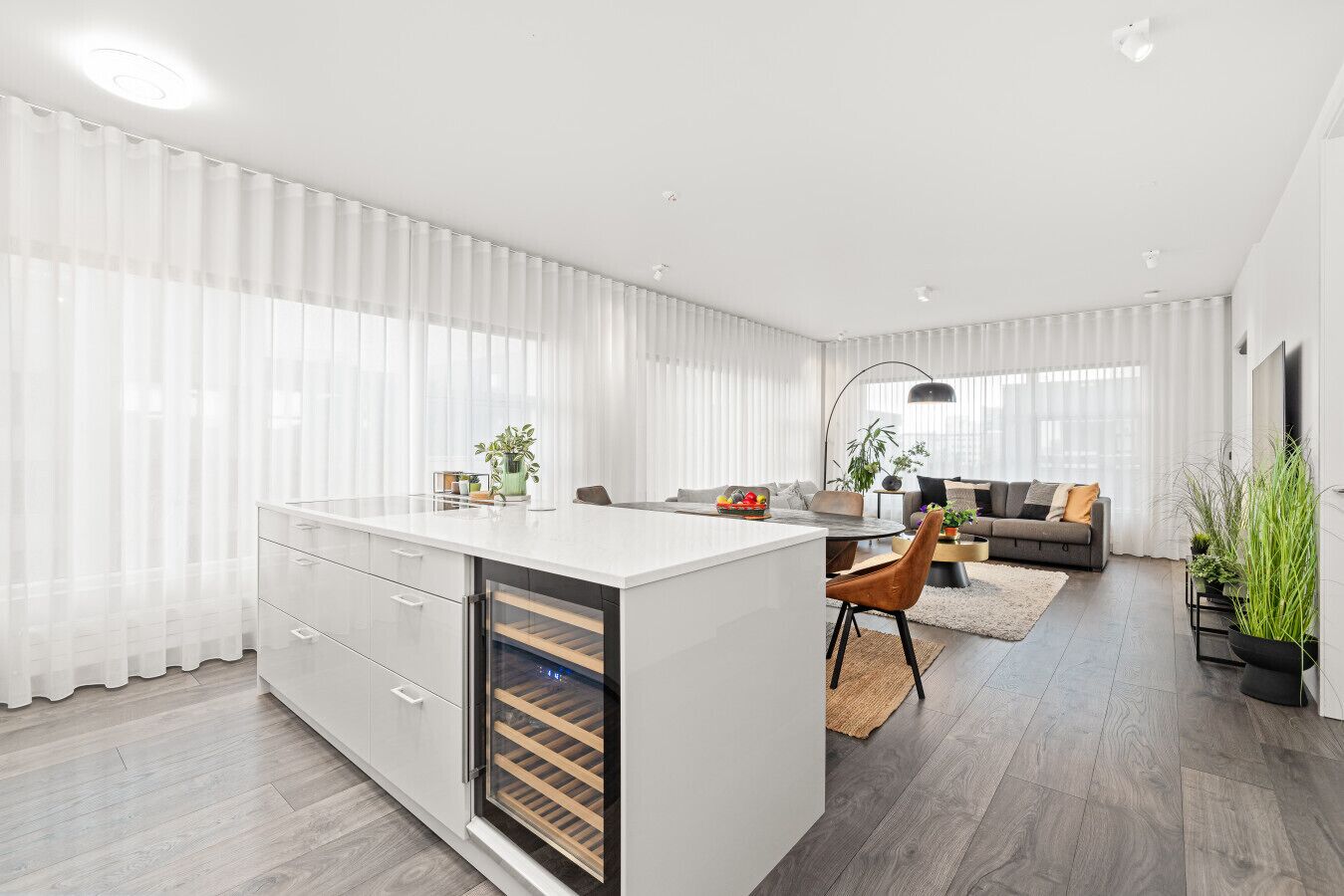 A modern kitchen with a central island, a dining area with a round table, and a living room with a sofa and a TV.