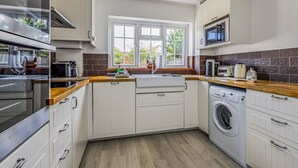 Una cucina moderna con mobili bianchi, forno integrato, microonde, lavello e lavatrice.