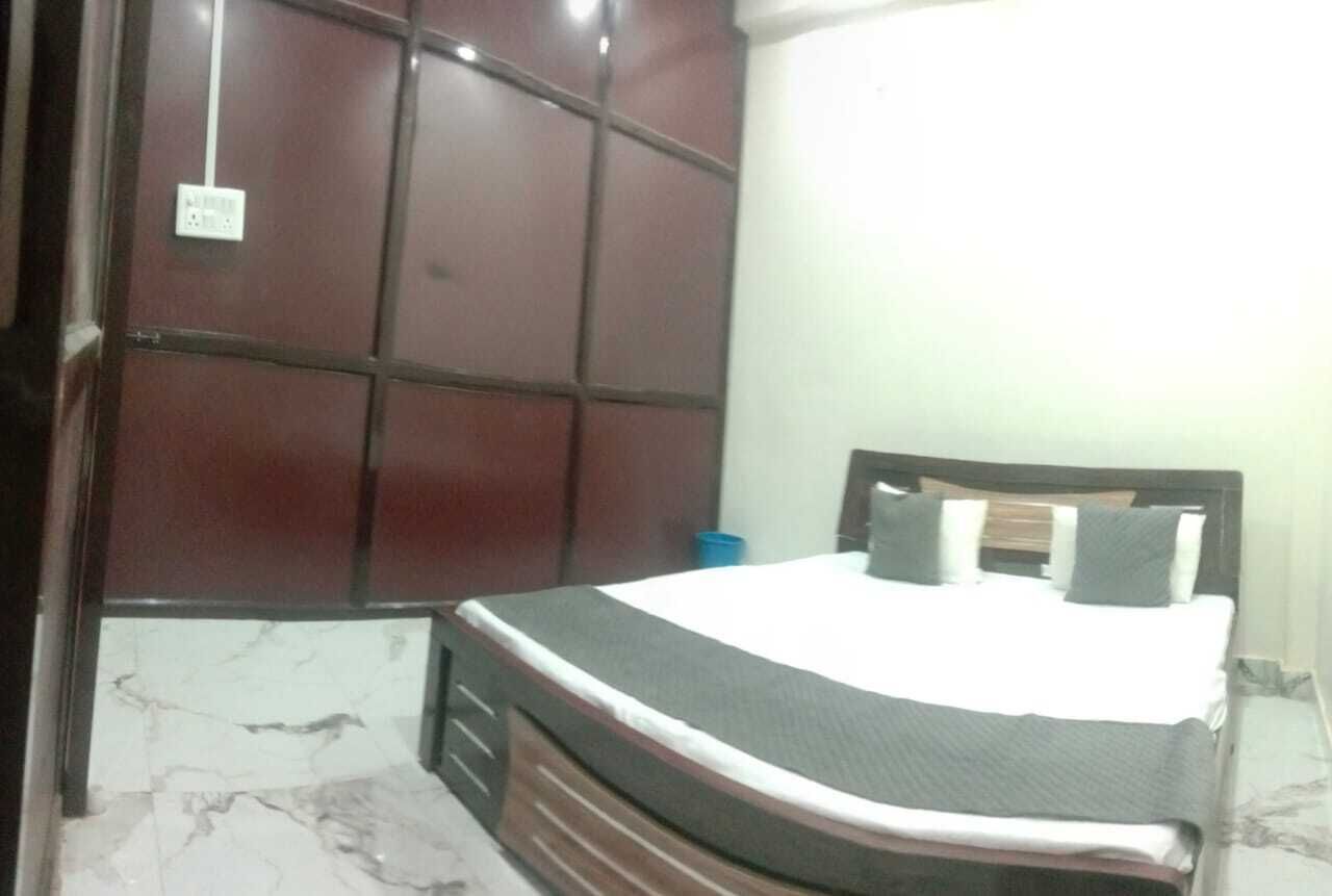 A bedroom with a bed, a wooden headboard, a marble floor, and a wall-mounted electrical outlet.