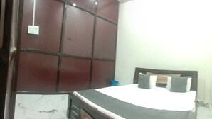 A bedroom with a bed, a wooden headboard, a marble floor, and a wall-mounted electrical outlet. - Hotel Seva & Restaurant (Agra)