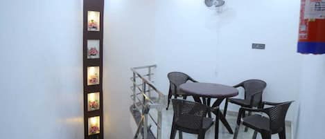 A dining area with a table and four chairs, a staircase with a handrail, and a wall-mounted fan.