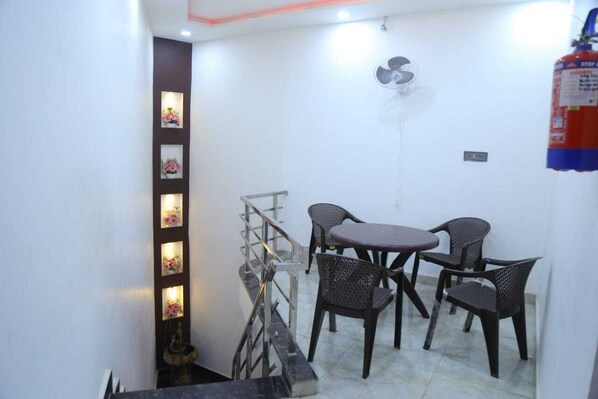 Un coin repas avec une table et quatre chaises, un escalier avec une rampe et un ventilateur fixé au mur.