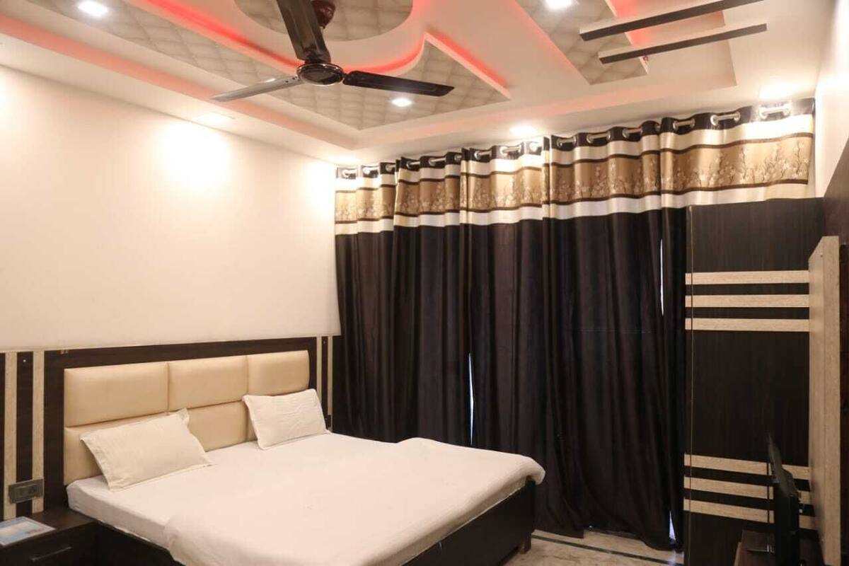 A hotel room with a bed, a nightstand, a ceiling fan, and a window with curtains.