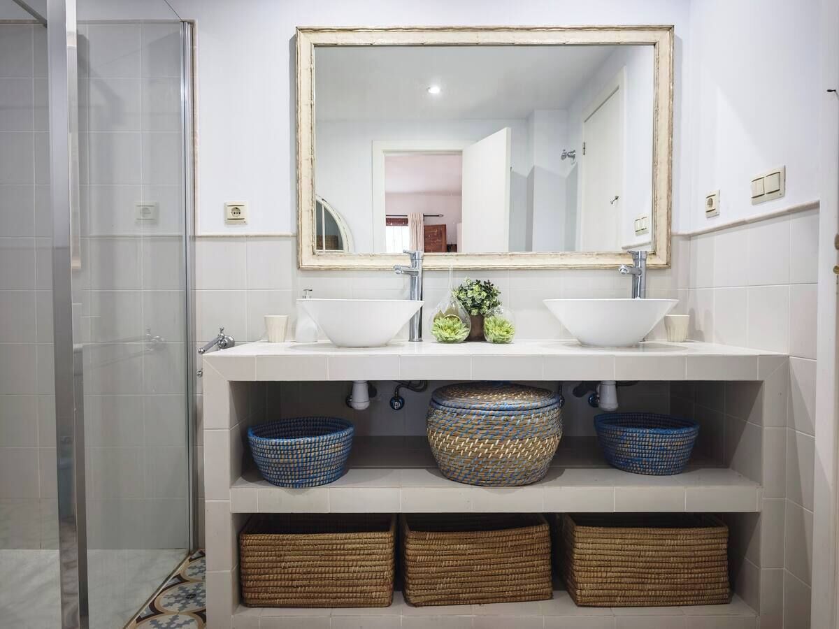 Een badkamer met twee wasbakken, een spiegel en drie gevlochten manden op planken.