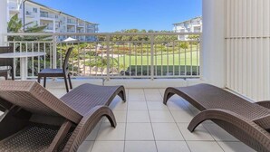 Un balcón con sillones de mimbre, una mesa y vistas a un campo de golf y edificios.
