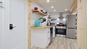 Eine kompakte Küche mit weißen Schränken, einer Holzarbeitsplatte und modernen Geräten, darunter eine Mikrowelle, ein Backofen und ein Kühlschrank.
