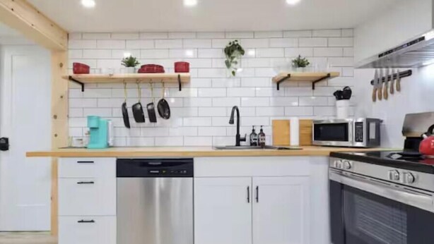 Eine moderne Küche mit weißen Schränken, Edelstahlgeräten und Holzregalen.