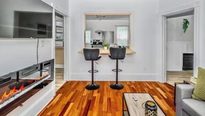A modern living room with a fireplace, wooden flooring, a TV, and a kitchen visible through an open doorway. - Victorian house (Sydney)