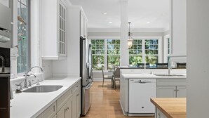 Una cocina moderna con armarios blancos, encimera de madera y vistas al exterior gracias a amplios ventanales.