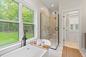 A modern bathroom with a bathtub, a glass shower enclosure, and a window with a view of greenery. - Dog-Friendly- EggHarbor w/ outdoor bar and grill (Egg Harbor)