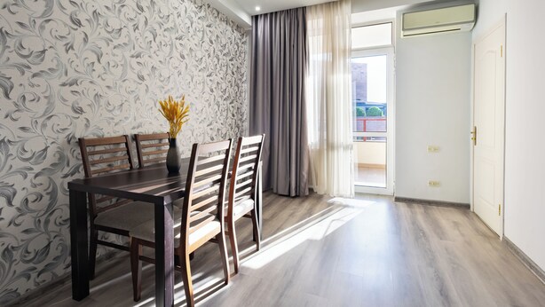Un coin repas avec une table et des chaises en bois, un papier peint à motifs et une vue sur l’extérieur par une porte.