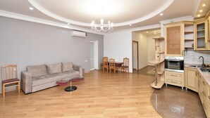 Un salon moderne avec un canapé gris, des chaises en bois, une table à manger et un coin cuisine doté de meubles en bois et d’une cuisinière.