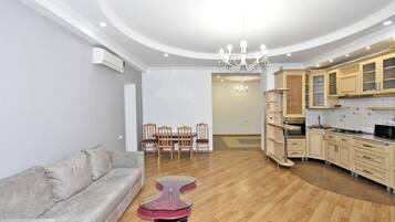 A modern living room with a grey sofa, a glass coffee table, and a dining area with wooden chairs.