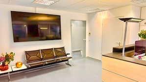 A modern waiting area with a bench, a flat-screen TV mounted on the wall, and a desk with a computer. - Donau-Iller Vermietung 24  (Neu-Ulm)