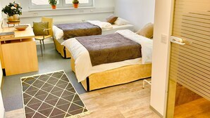 A hotel room with two beds, a desk, a chair, a small table, and a window with a view of greenery. - Donau-Iller Vermietung 24  (Neu-Ulm)