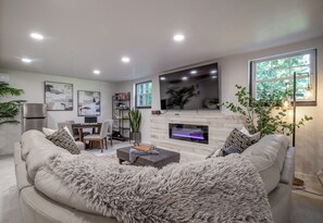 A modern living room with a fireplace, a sofa, and a dining area. - Pool, Pickleball, Poker, Ping-Pong! King beds! (Greer)