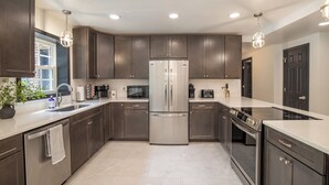 A modern kitchen with dark cabinets, stainless steel appliances, and a white countertop. - Pool, Pickleball, Poker, Ping-Pong! King beds! (Greer)