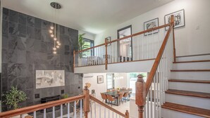 A spacious living area with a high ceiling, a fireplace, and a dining area with a wooden staircase. - Pool, Pickleball, Poker, Ping-Pong! King beds! (Greer)