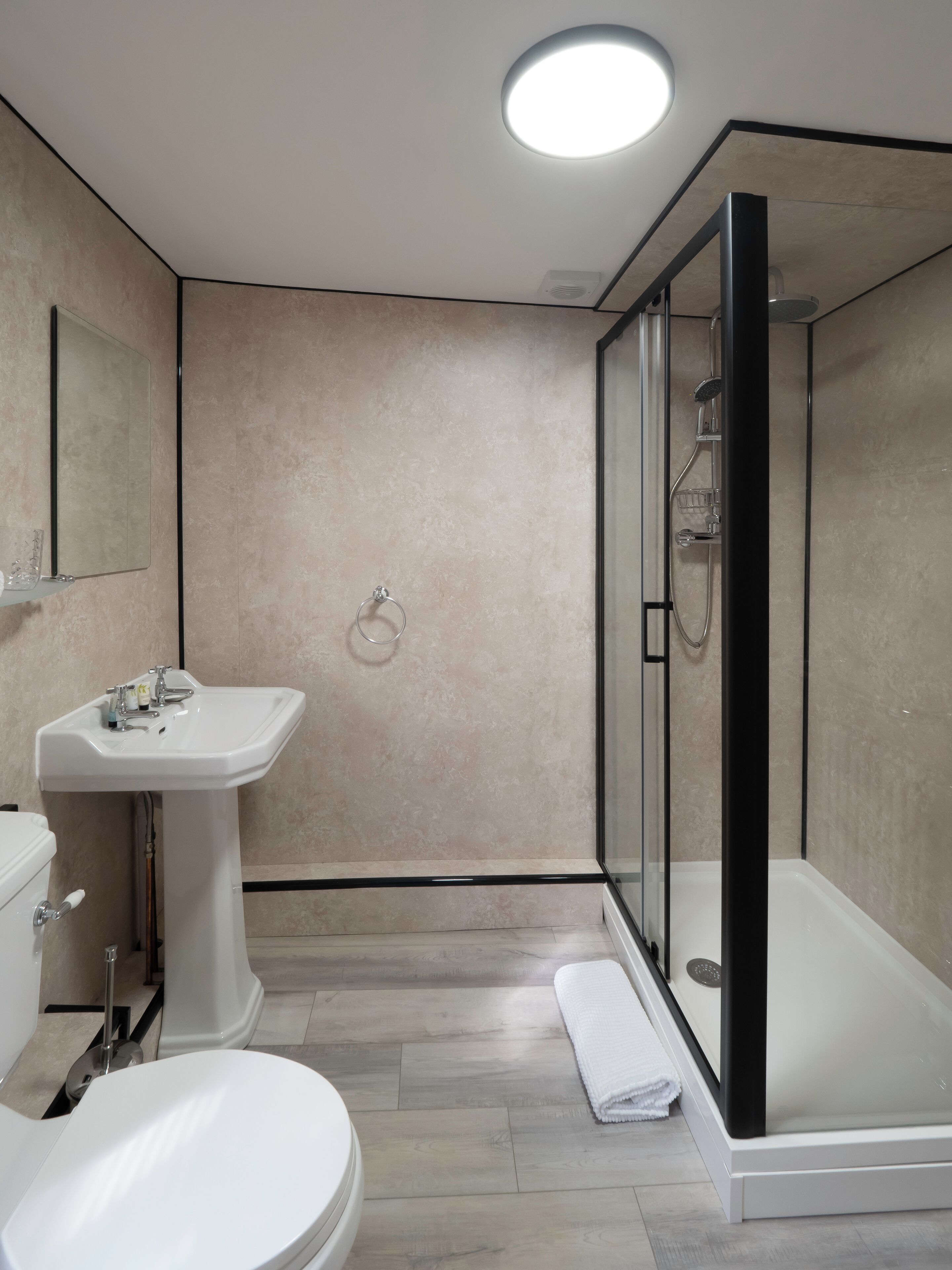 Un baño moderno con inodoro, lavamanos y ducha con mampara de vidrio.