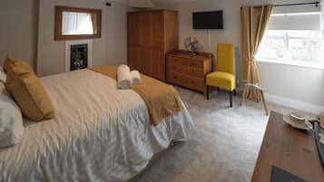 Ein Schlafzimmer mit einem Bett, einem Holzschrank, einem Fernseher, einem Ventilator, einem gelben Sessel, einem Glastisch und einem Fenster mit Vorhängen.