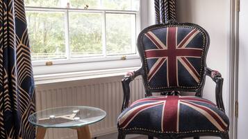 Una habitación con ventana, una silla con estampado de la bandera Union Jack y una mesa de vidrio.