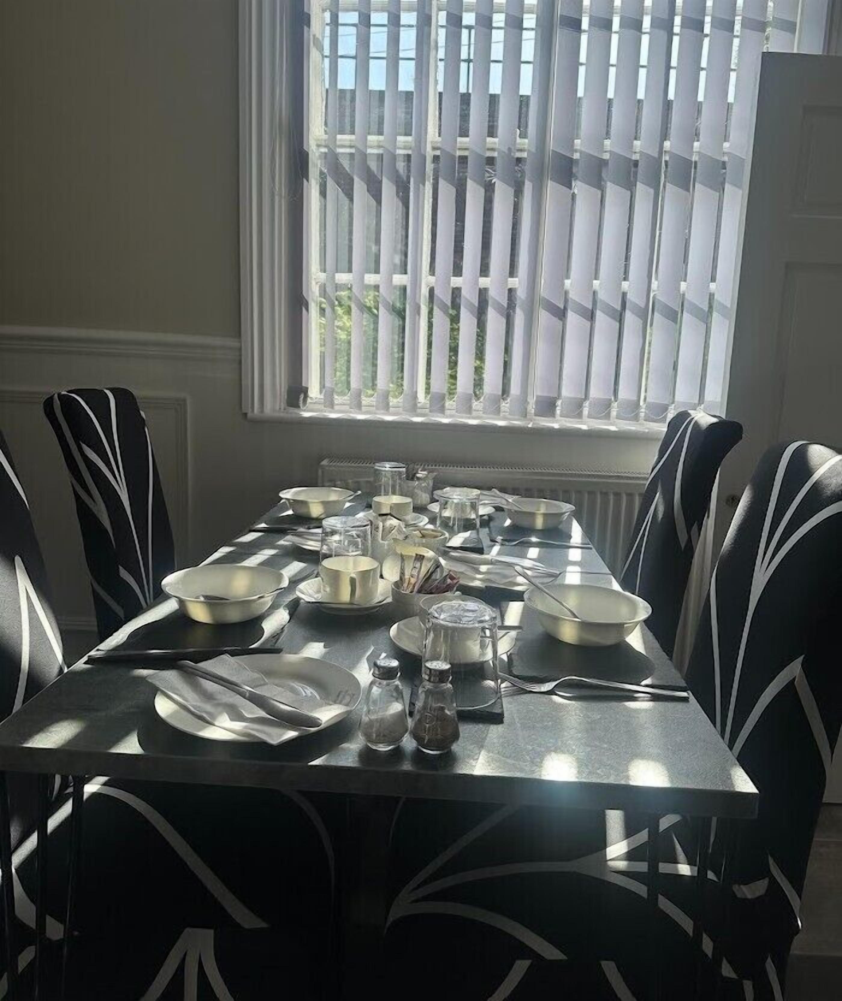 A dining table set with plates, bowls, and utensils, surrounded by chairs with a black and white pattern.