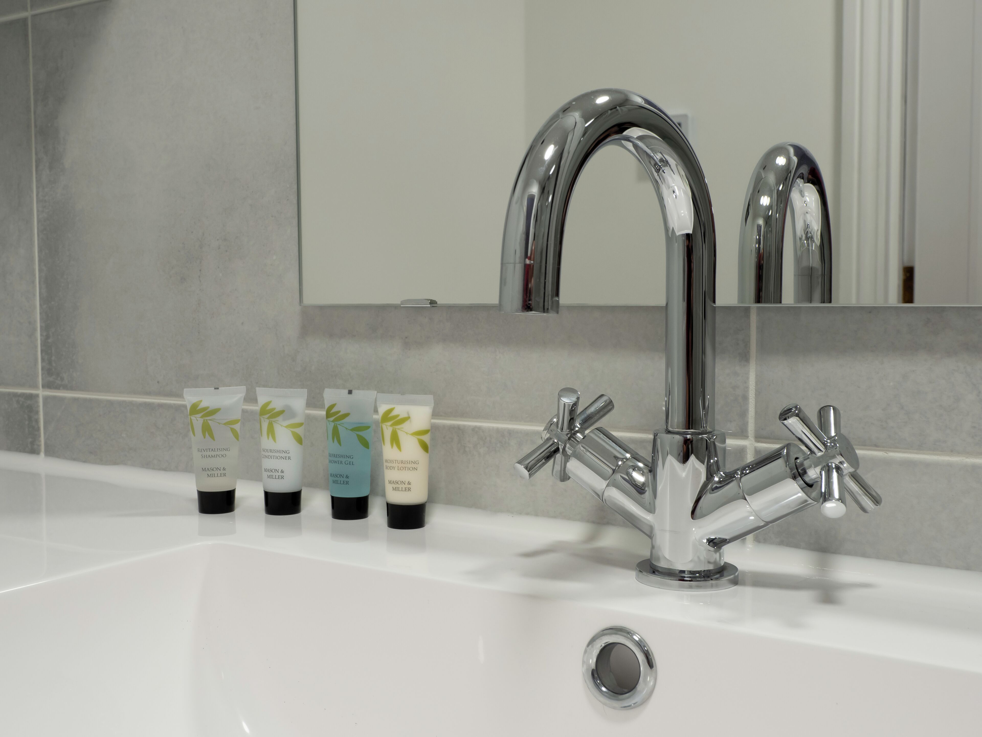 Un baño con un moderno grifo cromado, un espejo y tres artículos de aseo en el lavabo.