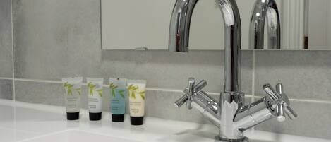 A bathroom with a modern chrome faucet, a mirror, and three toiletries on the sink.