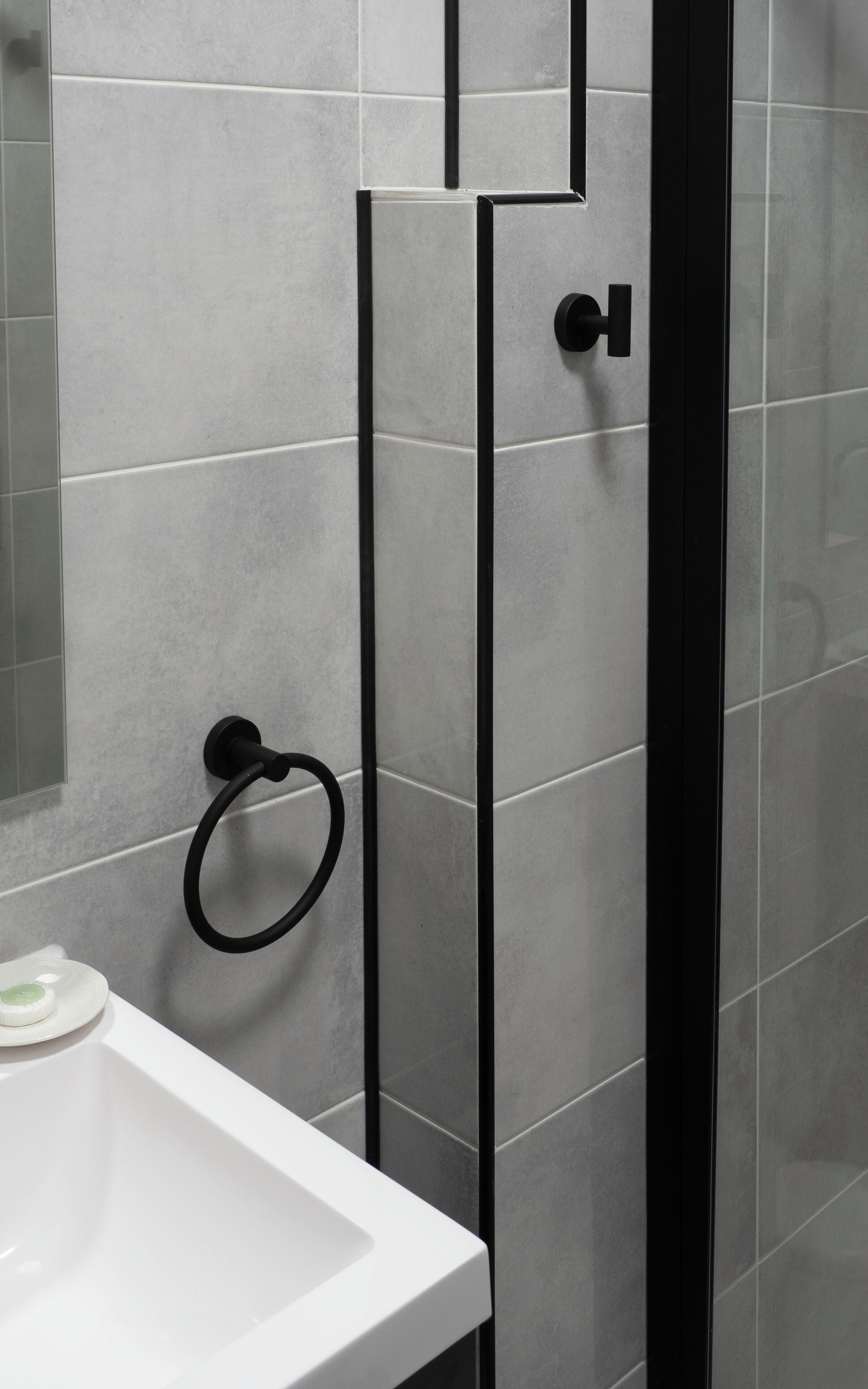 Een badkamer met een wit wastafelmeubel, een douchecabine van glas en grijze betegelde wanden.