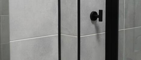 A bathroom with a white sink, a glass shower enclosure, and grey tiled walls.
