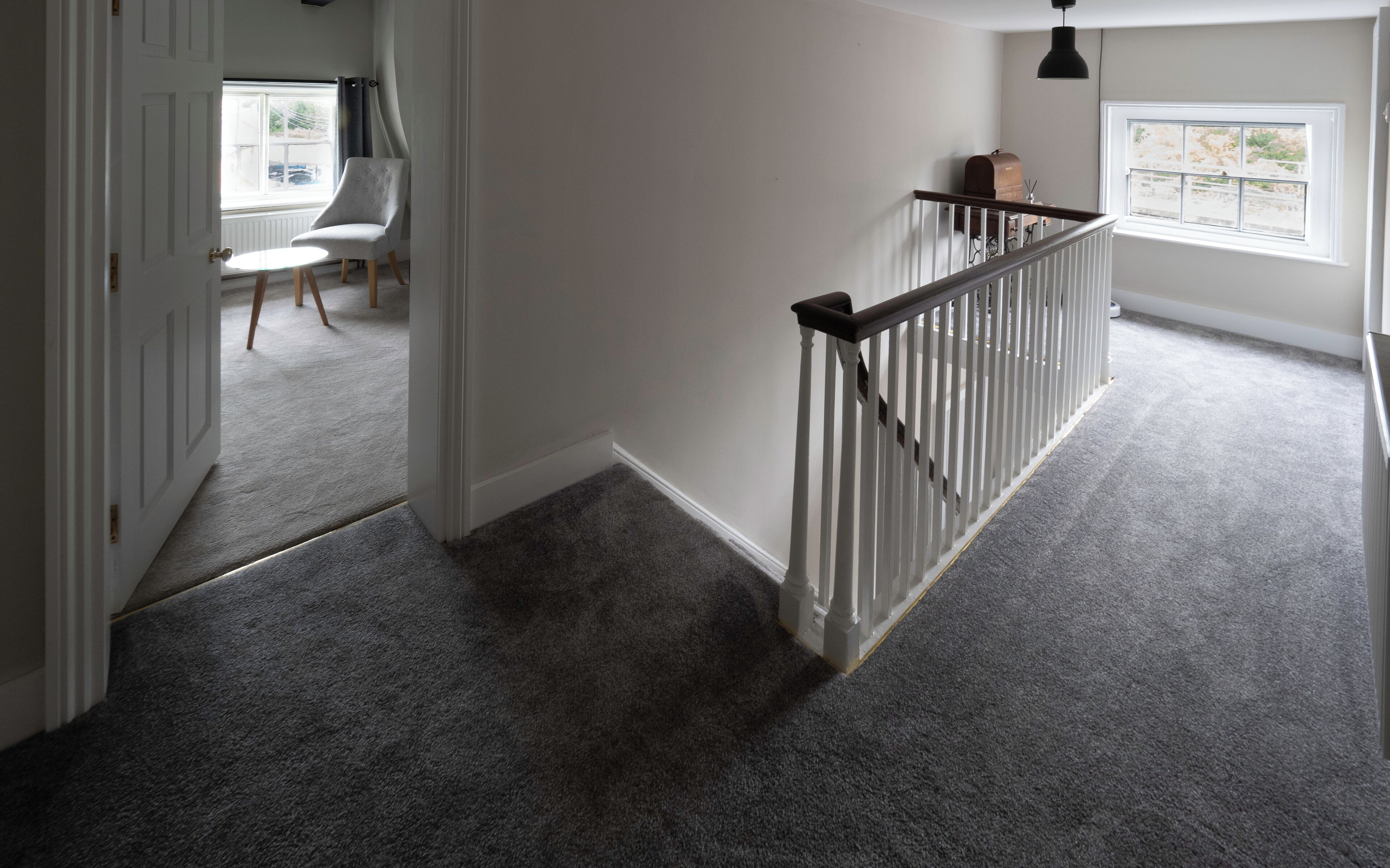 A hallway with a carpeted floor, a white door, a chair, and a window with a view of the outside.