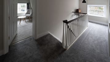 A hallway with a carpeted floor, a white door, a chair, and a window with a view of the outside.