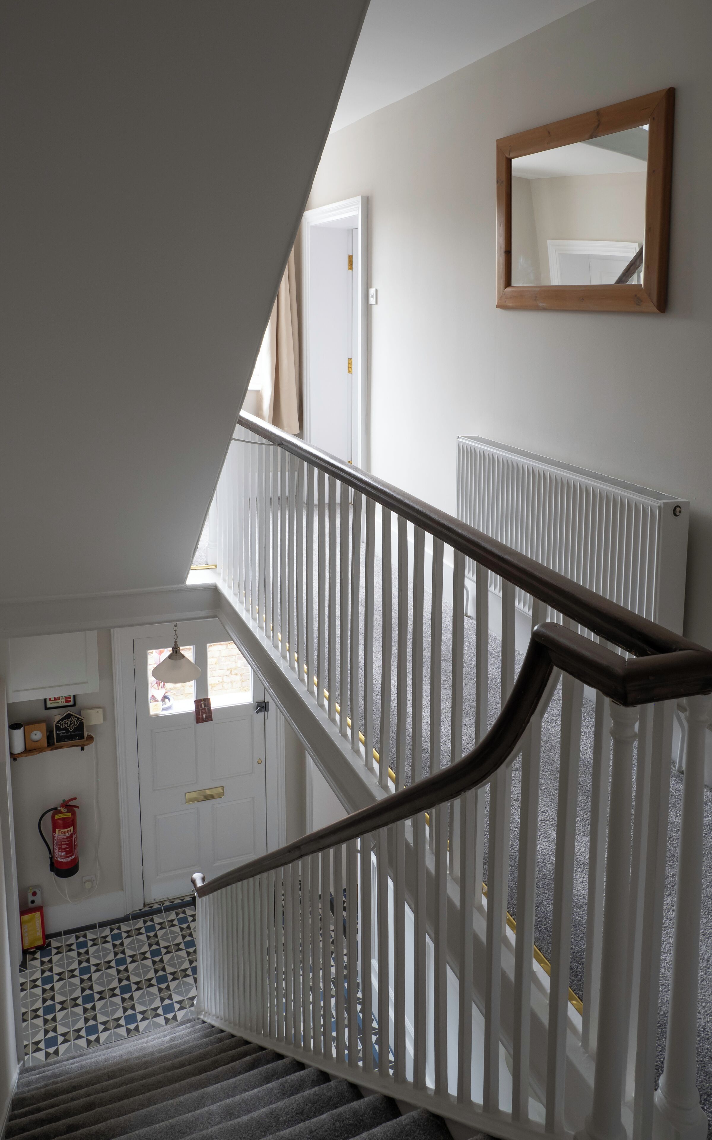 A staircase with white railings and a wooden handrail, leading to a door with a fire extinguisher and a small shelf with items on it.