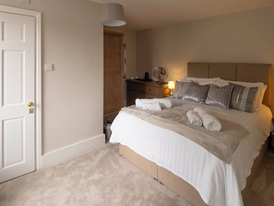 A neatly made bed with white linens and towels, a bedside lamp, and a wooden nightstand.
