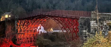A red metal bridge with a wooden walkway and a stone wall in the background.