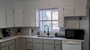 A kitchen with white cabinets, a black microwave, a dishwasher, and a window with blinds. - Ridgeline #1 Unique 2 bedroom house in Helper. (Helper)