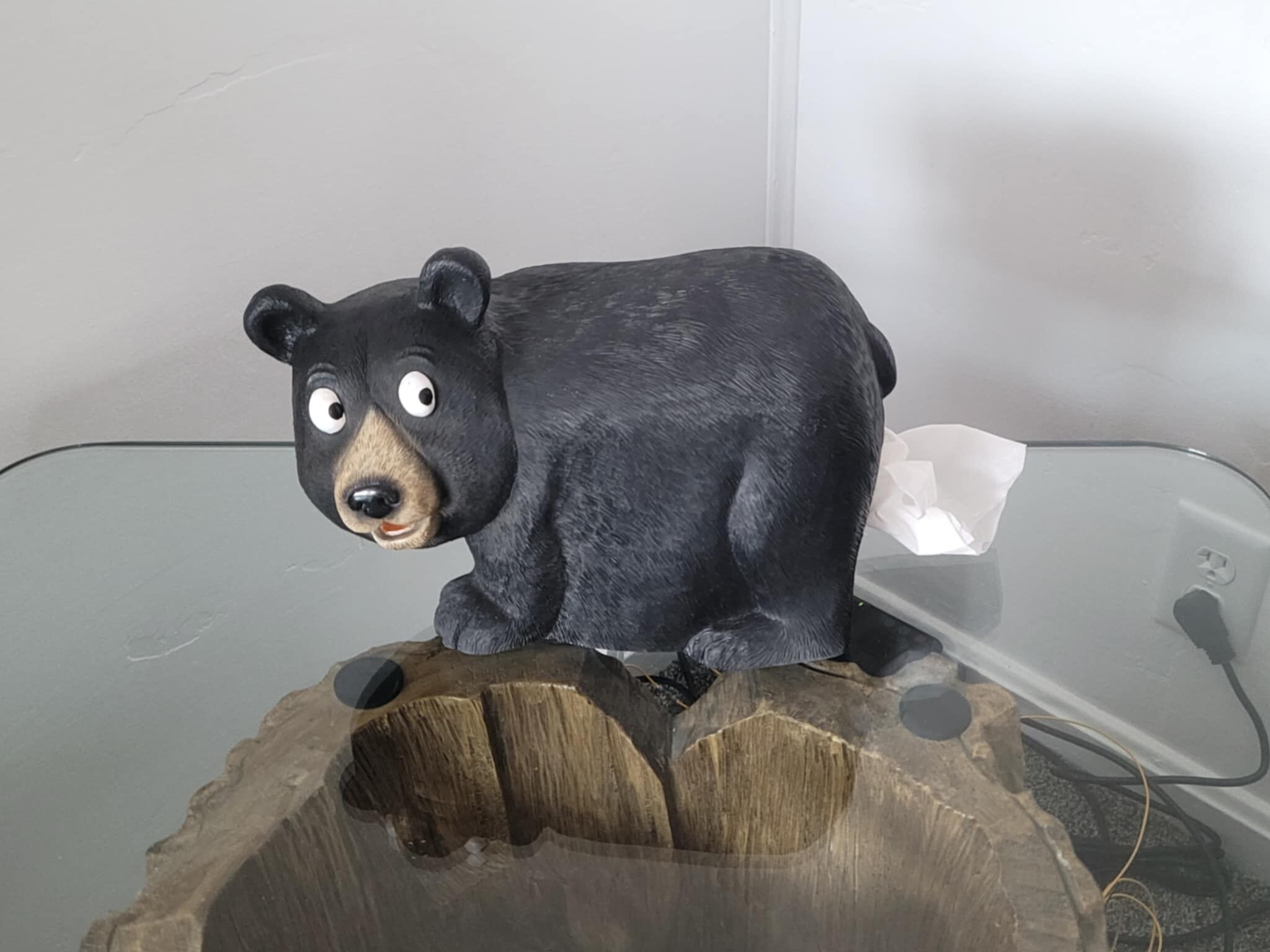 Een beeldje van een zwarte beer op een glazen tafel met een houten onderstel.