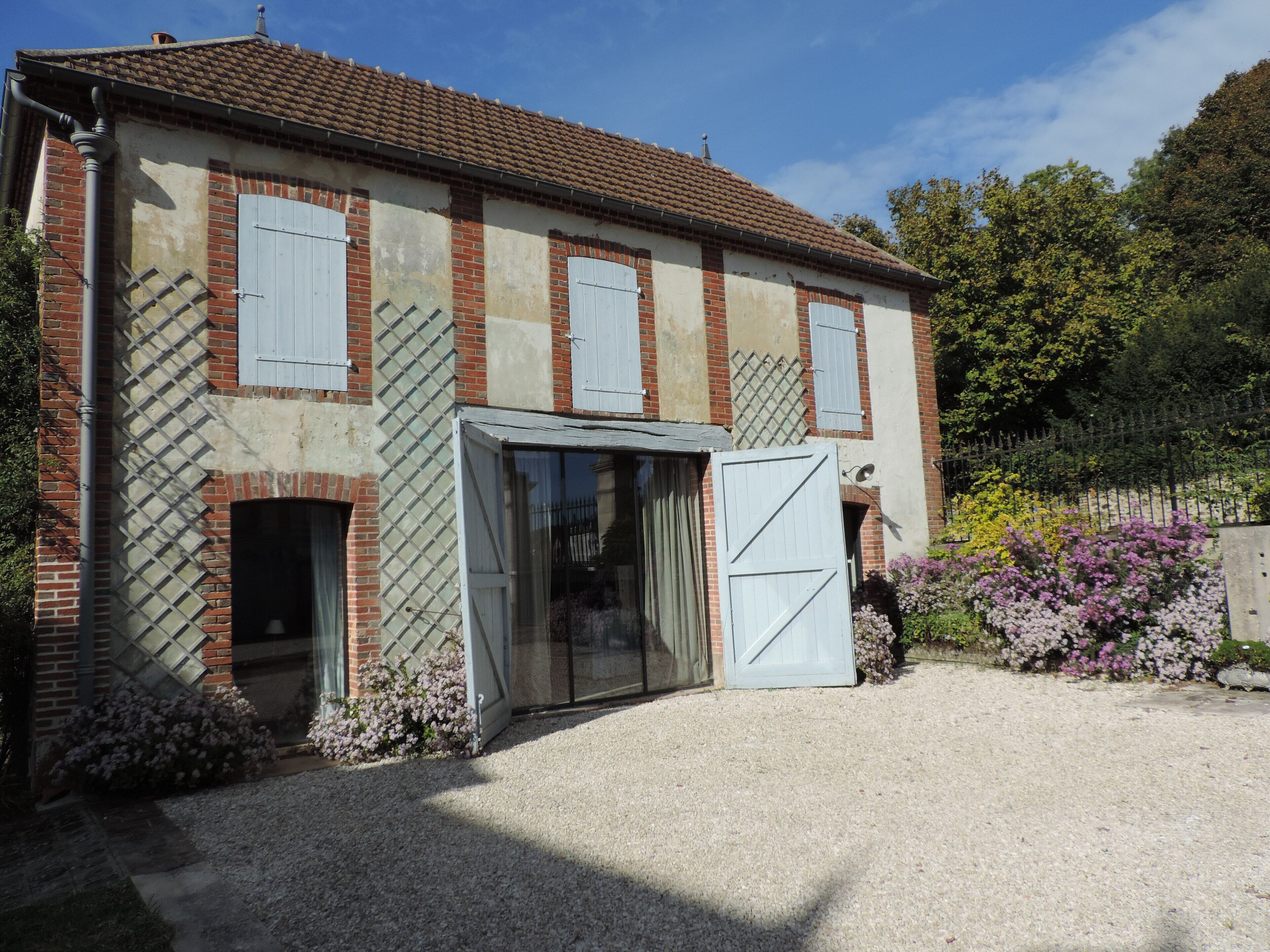 Un bâtiment à deux étages, doté d’un toit en tuiles, d’une allée gravillonnée et d’une clôture en bois.