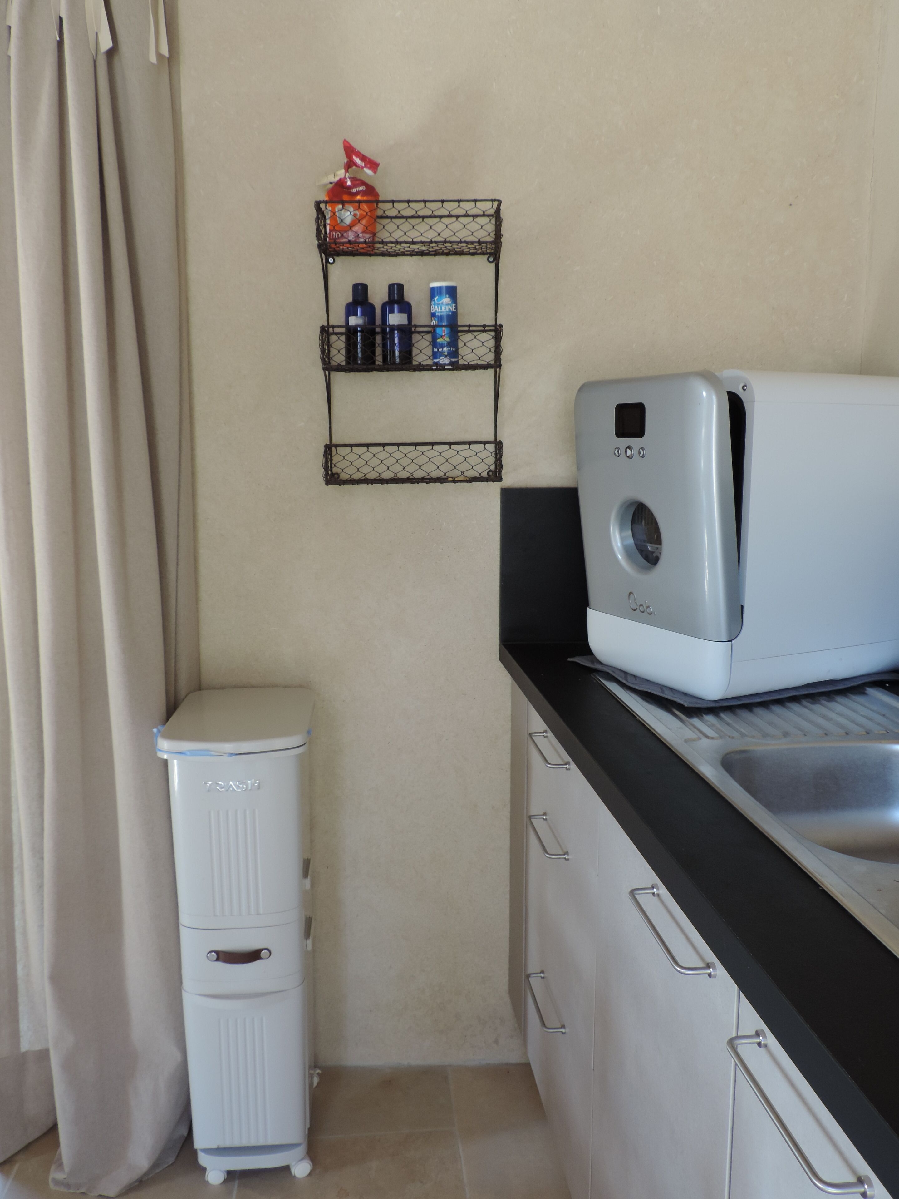 A compact kitchen with a washing machine, a small fridge, and a metal shelf with toiletries.
