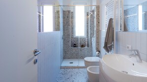 Un baño moderno con cabina de ducha de vidrio, inodoro y un lavamanos amplio.