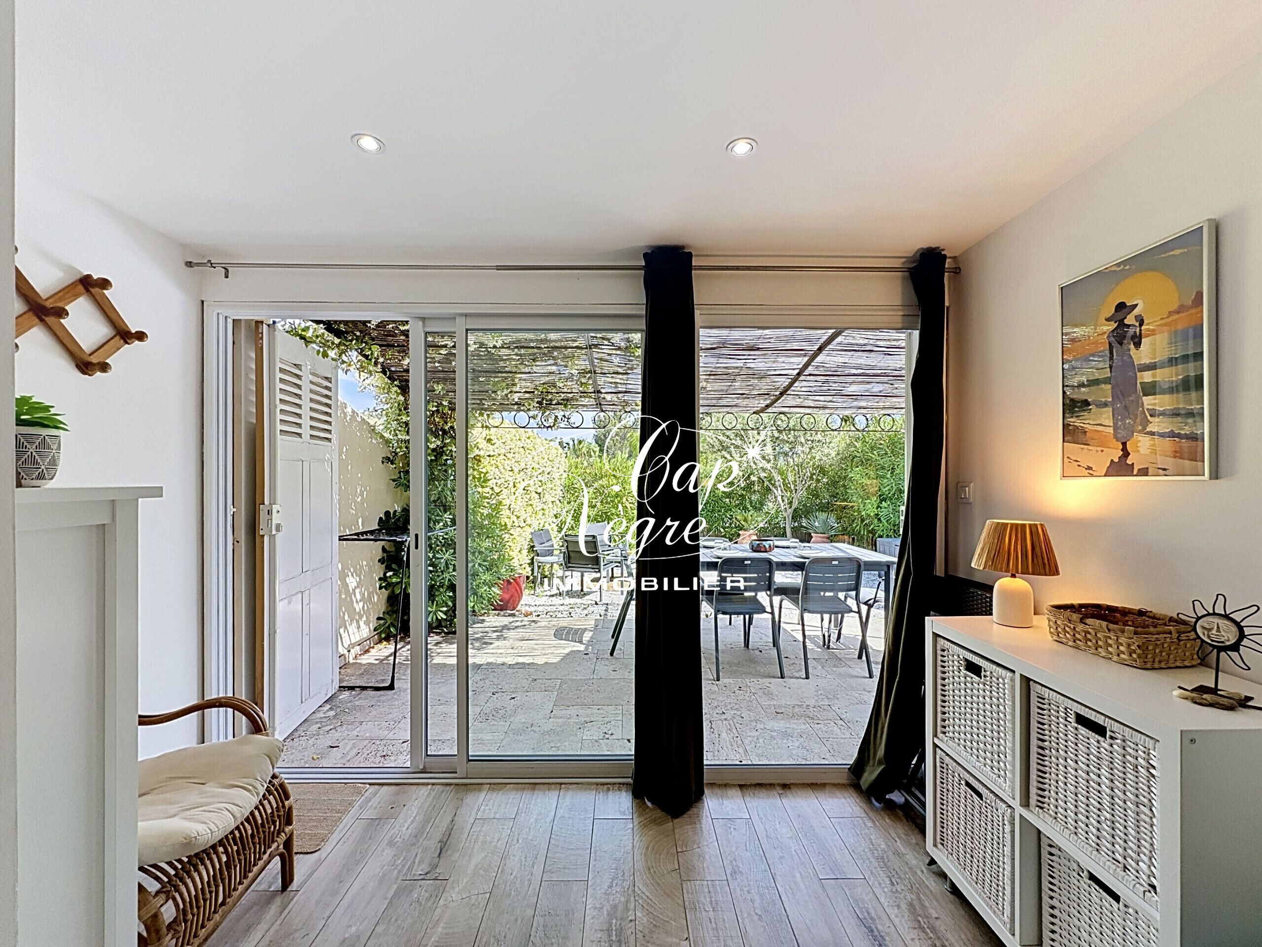 A room with a sliding glass door leading to an outdoor patio, a wicker sofa, a white cabinet with wicker baskets, and a framed picture on the wall.