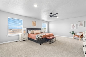 A bedroom with a bed, bedside tables, a ceiling fan, and large windows.