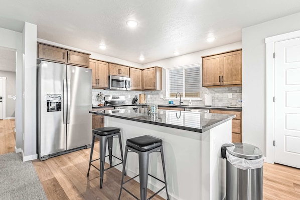 A modern kitchen with stainless steel appliances, wooden cabinets, and a central island with stools.