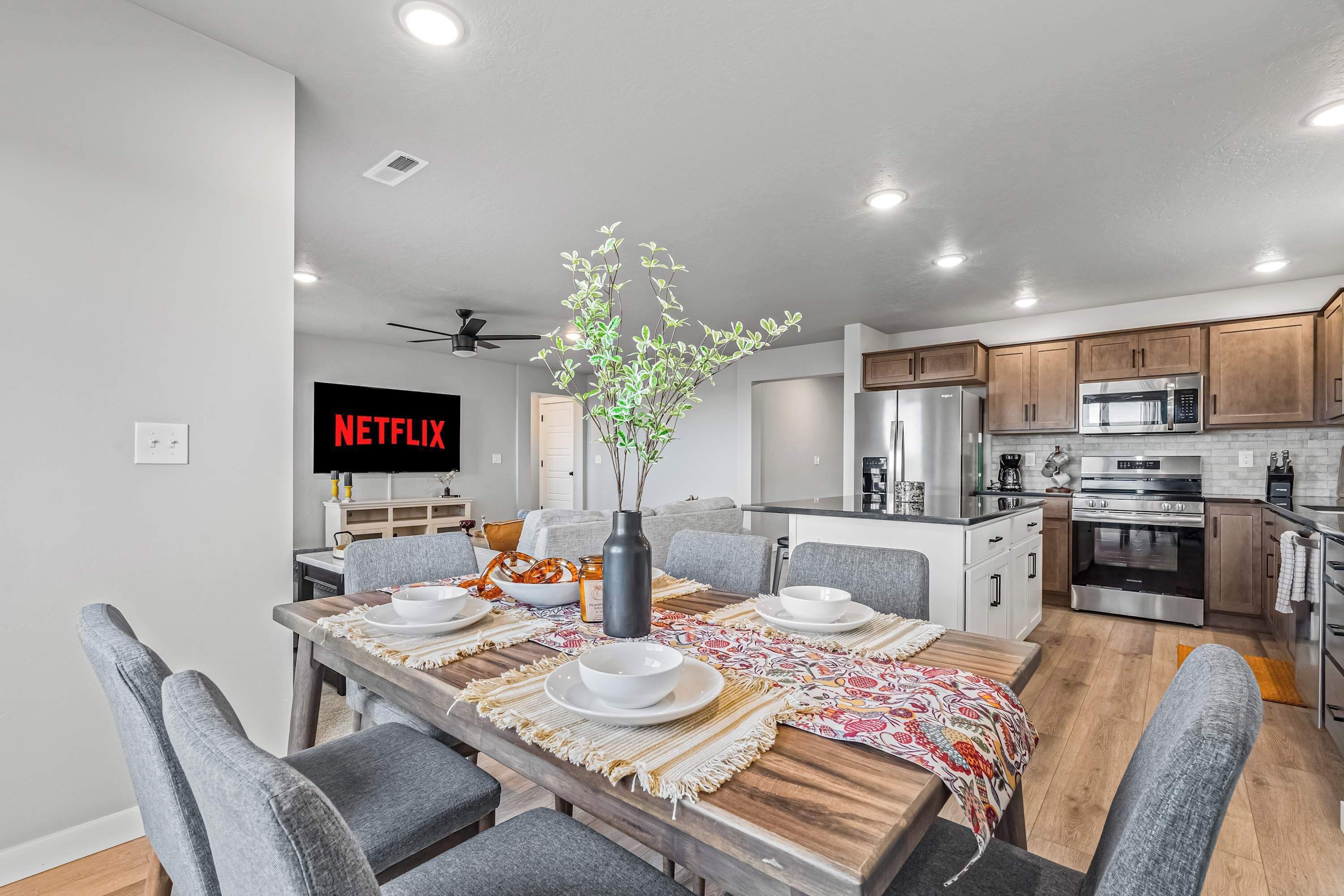A modern kitchen with a dining area, a flat-screen TV, and a ceiling fan.
