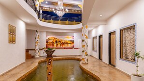 Un vaste atrium agrémenté d’un élément aquatique central, un balcon doté d’une balustrade et une grande fresque murale.